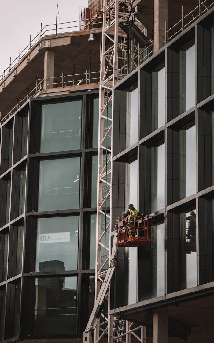 Construction workers on a suspended scaffold cleaning glass panels on a modern building in Dublin, Ireland.